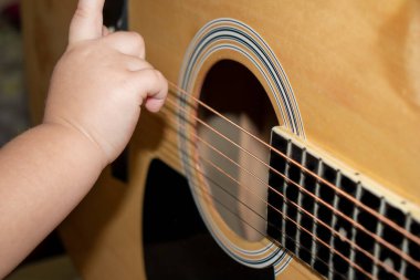 Bebek akustik gitarın tellerine uzanıyor.