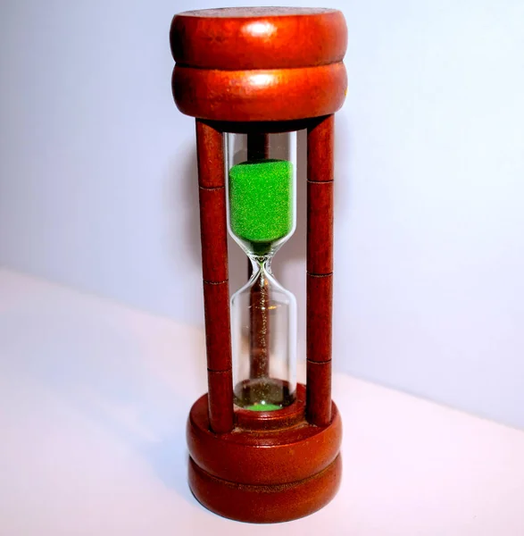 Hourglass with green sand on white background
