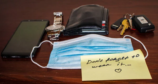 New reality. Picture of a phone, keys, wallet, watch surgical mask and note on side table