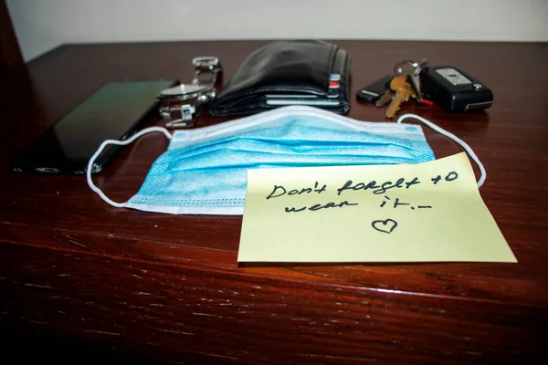 New reality. Picture of a phone, keys, wallet, watch surgical mask and note on side table