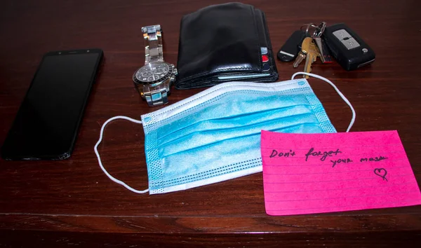 New reality. Picture of a phone, keys, wallet, watch surgical mask and note on side table