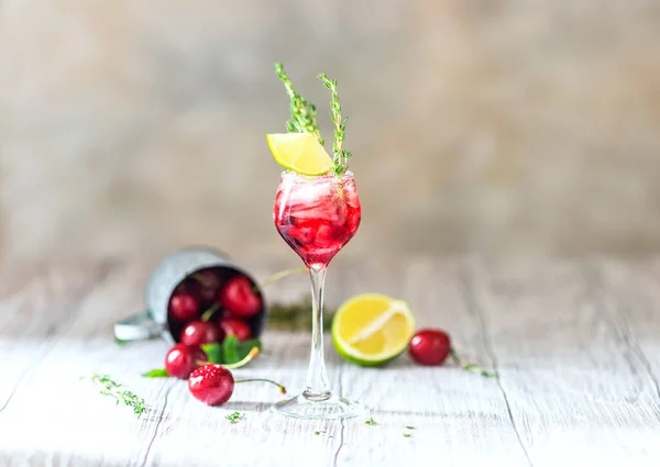 Cherry red cocktail with lime. Fresh summer cocktail with cherries, thyme and ice cubes. Selective focus