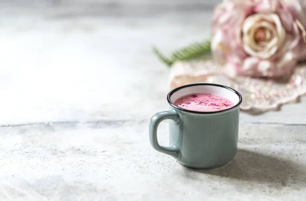 Ayurvedic rose moon milk. A trendy relaxing form of drink before bed. Milk with rose petals in a gray mug on a light concrete background. Selective focus, copy space.