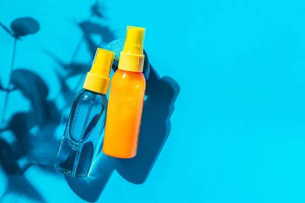 Cosmetic spray bottle blue and yellow with transparent liquid on a blue background. Spa cosmetics. Natural skincare. Copy space, top view.