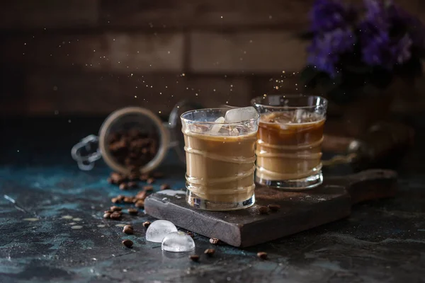 Splash of iced coffee in a glass glass and coffee beans on a brown background. Summer refreshing drink. Selective focus, copy space.
