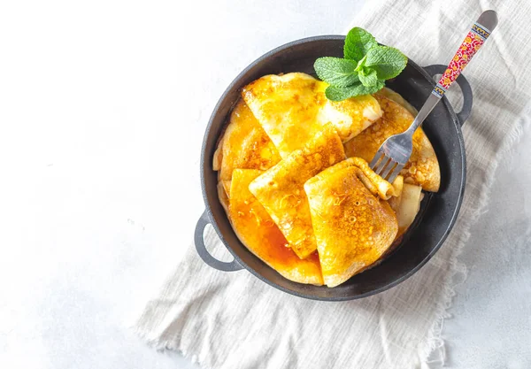 Crepes with Orange Sauce in a cast iron pan. Traditional French crepe Suzette with orange sauce. Flat lay, top view