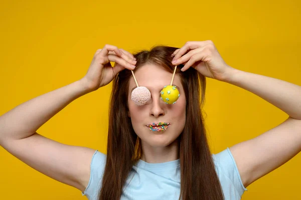 Joven europeo mujer juega con pastel pops en amarillo fondo — Foto de Stock