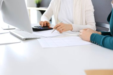 Muhasebeci mali durumu kontrol ediyor ya da vergi formları için hesap makinesi geliri ile sayıyor, eller yakın çekim. İş kadını ofisteki masada iş arkadaşıyla oturuyor ve çalışıyor. Denetim kavramı