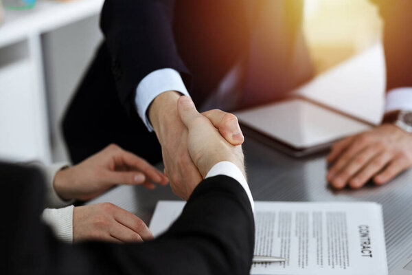 Деловые люди пожимают руки после подписания контракта в солнечном современном офисе. Концепция командной работы и рукопожатия