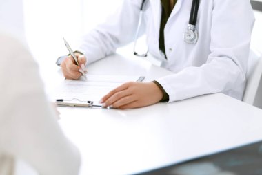 Kadın doktor ve hasta hastane muayenehanesinde oturuyor ve konuşuyor, yakın plan. İlaç kayıtlarını dolduran bir terapist. Tıp ve sağlık hizmetleri kavramı