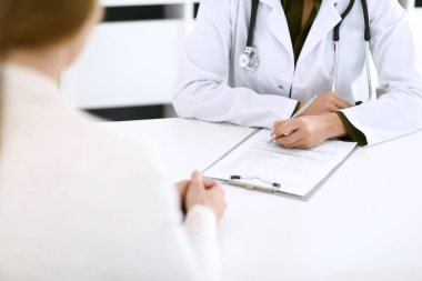 Kadın doktor ve hasta hastane muayenehanesinde oturuyor ve konuşuyor, yakın plan. İlaç kayıtlarını dolduran bir terapist. Tıp ve sağlık hizmetleri kavramı