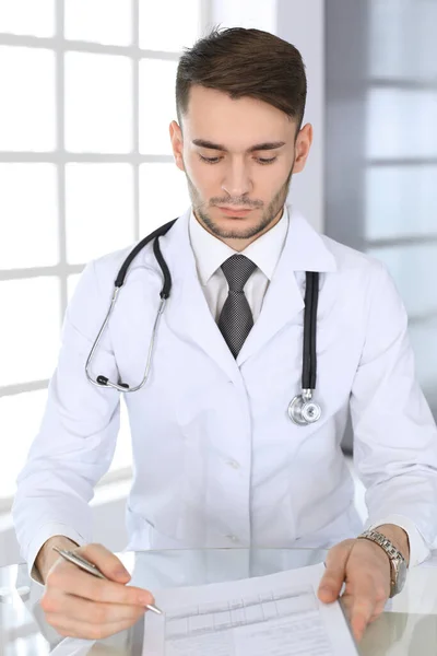 Homem médico preenchendo formulários de histórico de medicação enquanto estava sentado na mesa de vidro em um consultório médico ou clínica. Conceito de medicina e saúde — Fotografia de Stock