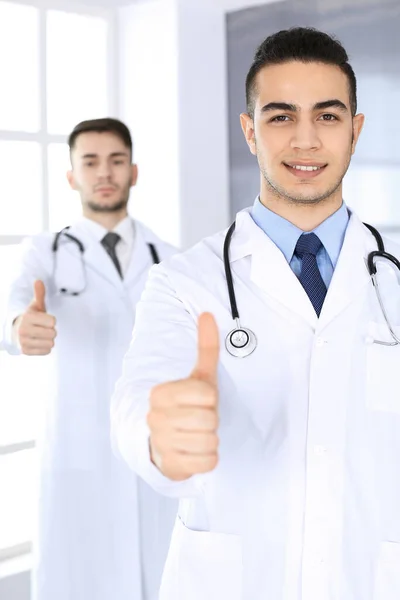 Arabische arts toont OK teken met duimen omhoog met Kaukasische collega in het medisch kantoor of kliniek. Diverse artsen team, beste behandeling, geneeskunde en gezondheidszorg concept — Stockfoto