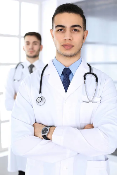 Arabski lekarz stojący z białym kolegą w gabinecie medycznym lub klinice. Różnorodny zespół lekarzy, koncepcja medycyny i opieki zdrowotnej — Zdjęcie stockowe