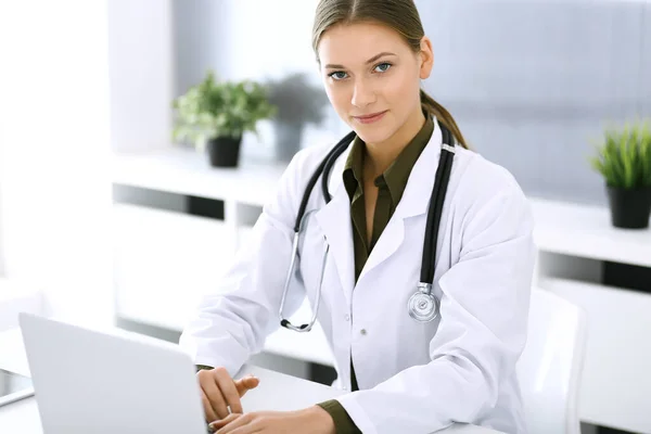 의사 가 사무실 책상에 앉아 있는 동안 노트북 컴퓨터로 타이핑을 하고 있습니다. 의사가 일하는 여성. 의학 과 건강 관리에 관한 자료 — 스톡 사진