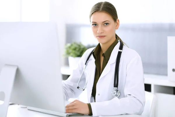 Médico escribiendo en el ordenador PC mientras está sentado en el escritorio en la oficina del hospital. Mujer médica en el trabajo. Datos en medicina y asistencia sanitaria — Foto de Stock