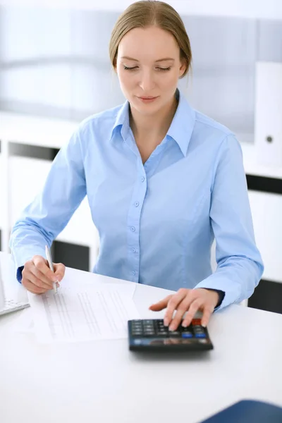 会计师核对财务报表或以计算器收入计算报税表.女商人坐在办公室的桌子前工作.审计概念 — 图库照片