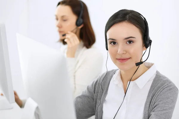 Centro de llamadas. Hermosa recepcionista mujer sentada en auriculares en la oficina de servicio al cliente. Grupo de operadores en el trabajo. Concepto empresarial —  Fotos de Stock