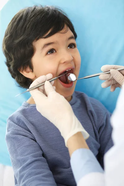 Pequeño chico árabe sentado en la silla dental con la boca abierta durante la revisión oral mientras que el médico. Visita al consultorio del dentista. Concepto de medicina y estomatología — Foto de Stock