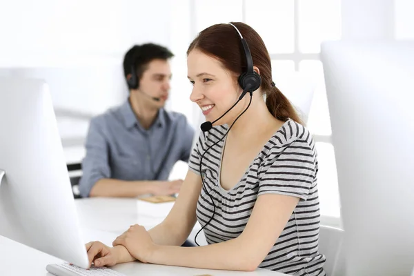 Group of operators at work. Call center. Focus on beautiful woman receptionist in headset at customer service. Business concept and casual striped clothing style — Stock Photo, Image