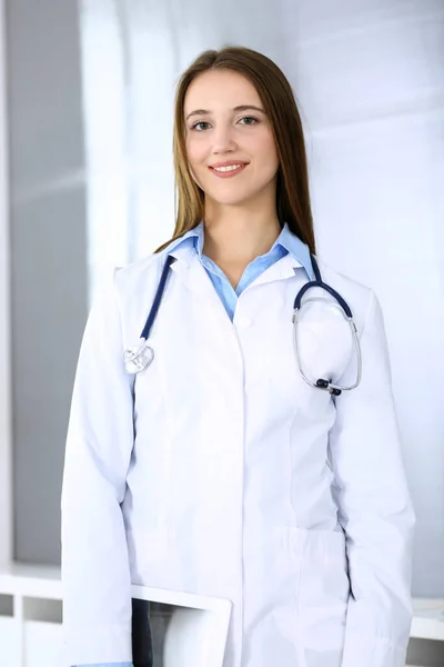 Doktor kadın mutlu ve neşeliyken arka planda hastane ofisinde dikiliyordu. Tıp ve sağlık hizmetleri kavramı — Stok fotoğraf