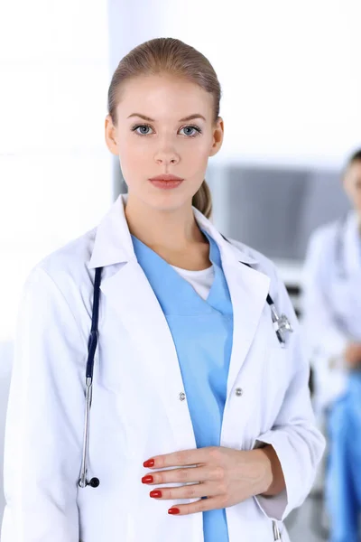 Doktorka stojí na pohotovosti v nemocnici s kolegyní v pozadí. Lékař v práci, studiový portrét. Koncepce medicíny a zdravotní péče — Stock fotografie