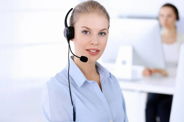 Llama a la oficina central. Hermosa mujer rubia usando computadora y auriculares para consultar a los clientes en línea. Grupo de operadores que trabajan como ocupación de servicio al cliente. Concepto gente de negocios — Foto de Stock