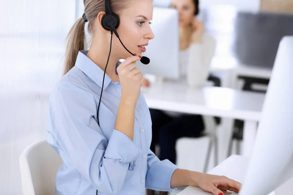 Звони в офис центра. Блондинка, использующая компьютер и гарнитуру для онлайн-консультаций с клиентами. Группа операторов, работающих в сфере обслуживания клиентов. Концепция бизнеса — стоковое фото