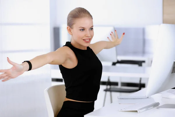Business woman happy and excited while working with computer in modern office. Secretary or female lawyer looks beautiful in black dress. Raised arms because of emotion. Business people concept