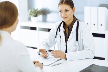 Kadın doktor ve hasta hastane ofisinde oturuyor ve konuşuyor. Yeşil renkli bluz terapiste uygun.