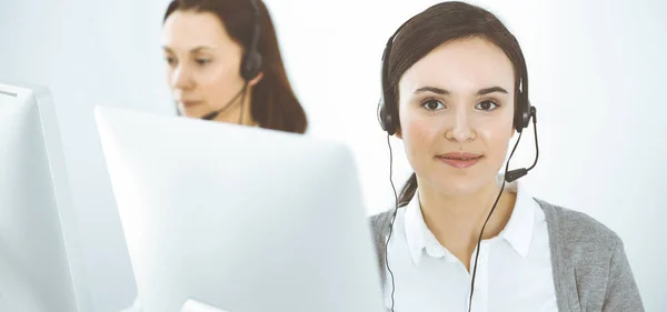 Zadzwoń do centrum. Nieformalnie ubrana kobieta pracująca w słuchawkach z różnymi kolegami w biurze. Koncepcja przedsiębiorstwa — Zdjęcie stockowe