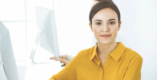 Affärskvinna i senapsfärgad blus tittar på kameran på kontoret, headshot — Stockfoto