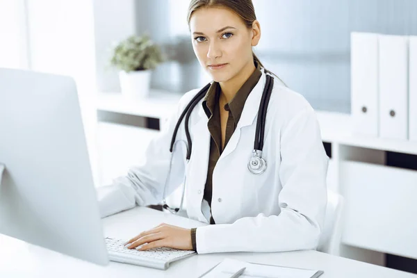 Mulher-médico digitando no computador pc enquanto sentado na mesa no escritório do hospital. Dados em medicina e cuidados de saúde — Fotografia de Stock