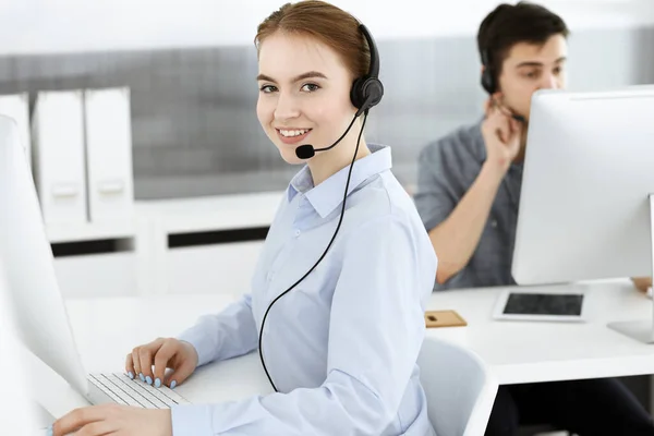 Mulher jovem usando fone de ouvido e computador enquanto conversa com clientes on-line. Grupo de operadores de call center no trabalho. Conceito de negócio — Fotografia de Stock