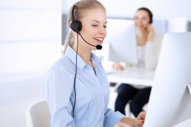 Merkezi ara. İnternette müşterilere danışmak için bilgisayar ve kulaklık kullanan güzel sarışın kadın. Müşteri hizmetleri işgali olarak çalışan bir grup operatör. İş adamları konsepti