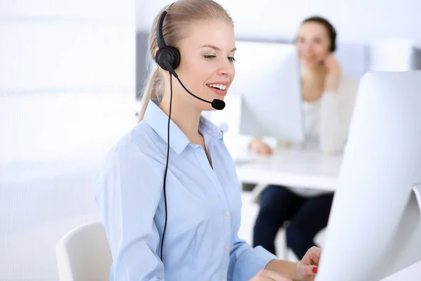 Llama a la oficina central. Hermosa mujer rubia usando computadora y auriculares para consultar a los clientes en línea. Grupo de operadores que trabajan como ocupación de servicio al cliente. Concepto gente de negocios —  Fotos de Stock