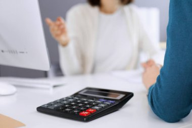 Mali durumu kontrol eden ya da vergi formları için hesap makinesinin geliri ile sayan, elleri yakın çekim. İş kadını, iş yerinde iş arkadaşıyla birlikte mavi tonda oturuyor. Vergi ve