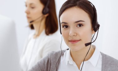 Merkezi ara. Ofisteki çeşitli iş arkadaşlarıyla kulaklık takan sıradan giyinmiş bir kadın. İş konsepti