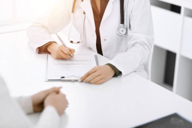 Güneşli klinikteki tıbbi muayenede oturan ve konuşan kimliği belirsiz kadın-doktor ve kadın hasta, yakın plan. İlaç geçmişini dolduran bir terapist. Tıp konsepti