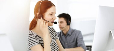 İnternette müşterilerle konuşurken kulaklık ve bilgisayar kullanan sıradan giyinmiş genç bir kadın. Güneşli ofiste çalışan bir grup operatör. Çağrı merkezi