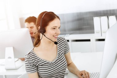 İnternette müşterilerle konuşurken kulaklık ve bilgisayar kullanan sıradan giyinmiş genç bir kadın. Güneşli ofiste çalışan bir grup operatör. Çağrı merkezi