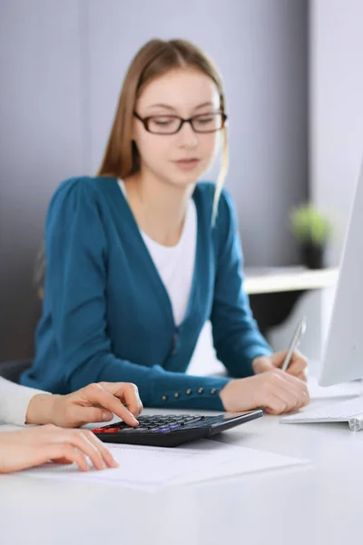 Contabilista verificando ficha financeira ou contando por calculadora de renda para a forma de imposto, mãos close-up. Mulher de negócios sentada e trabalhando com colega na mesa no escritório tonificada em azul. Impostos e — Fotografia de Stock