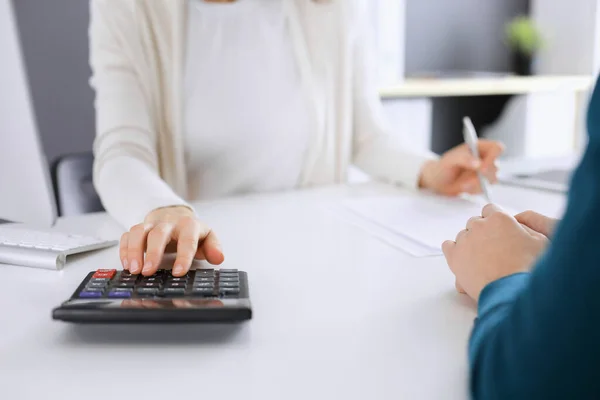 Contabile controllare il bilancio o conteggio dal reddito calcolatrice per la forma fiscale, mani primo piano. Donna d'affari seduta e che lavora con un collega alla scrivania in ufficio tonica in blu. Imposte e — Foto Stock