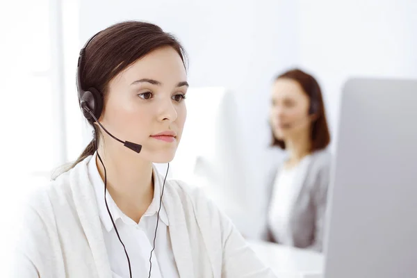 Call center. Casual dressed woman sitting in headset at customer service office. Group of operators at work. Business concept