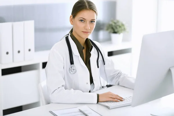 Woman-doctor typing on pc computer while sitting at the desk in hospital office. Physician at work. Data in medicine and healthcare