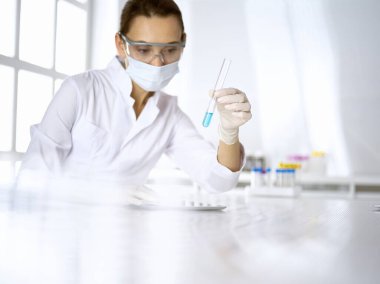 Kadın laboratuvar asistanı mavi sıvıyla test tüpünü analiz ediyor. Tıp, sağlık ve araştırma konsepti