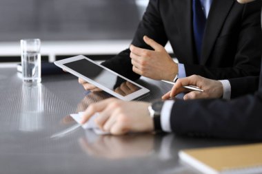 İşadamı tablet bilgisayar kullanıyor ve iş arkadaşı ya da ortağıyla modern ofiste cam masada çalışıyor. Yakın plan. Toplantıda bilinmeyen iş adamları var. Takım çalışması ve ortaklık kavramı
