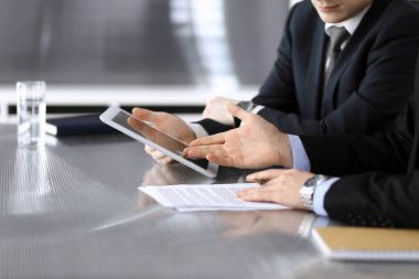 İşadamı tablet bilgisayar kullanıyor ve iş arkadaşı ya da ortağıyla modern ofiste cam masada çalışıyor. Yakın plan. Toplantıda bilinmeyen iş adamları var. Takım çalışması ve ortaklık kavramı