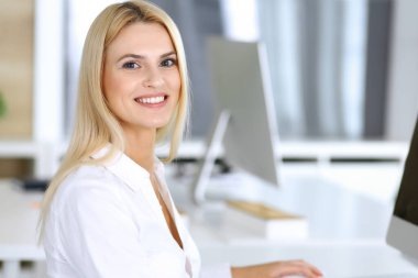 Modern ofisteki işyerinde bilgisayar kullanan bir iş kadını. Sekreter ya da kadın avukat kameraya bakıyor ve mutlu gülümsüyor. Zevk ve başarı için çalışmak
