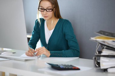 Muhasebeci mali durumu kontrol ediyor ya da vergi formları için hesap makinesi geliri ile sayıyor, eller yakın çekim. Ofisteki masada oturan ve çalışan bir iş kadını. Denetim kavramı